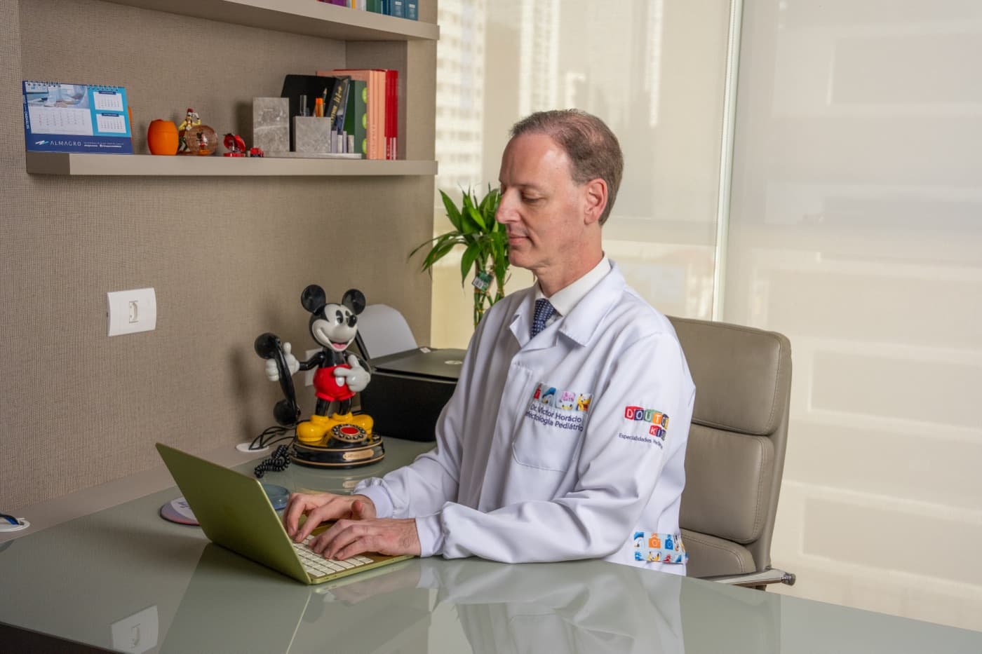 Dr. Victor Horácio trabalha no laptop em sua mesa no consultório